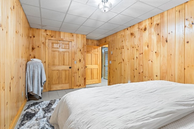 bedroom with a drop ceiling, light tile patterned floors, and wood walls