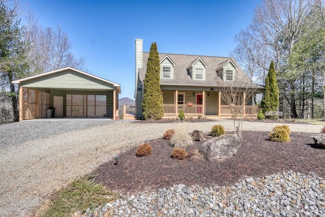 cape cod-style house featuring gravel driveway, a chimney, a porch, and a carport