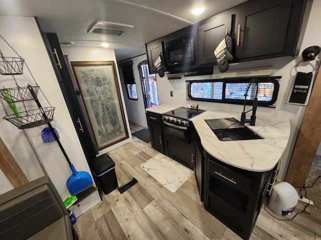 kitchen with light stone counters, visible vents, light wood-style flooring, black microwave, and dark cabinetry