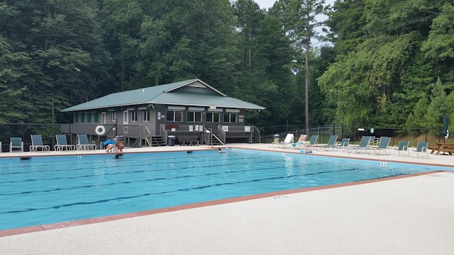 pool with a patio, a wooded view, and fence