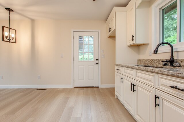 interior space with hanging light fixtures, white cabinets, sink, light stone countertops, and light hardwood / wood-style flooring