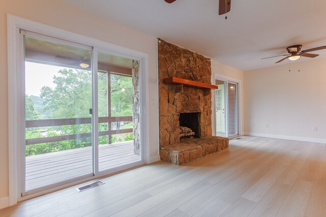 unfurnished living room with a stone fireplace, light wood-type flooring, and ceiling fan