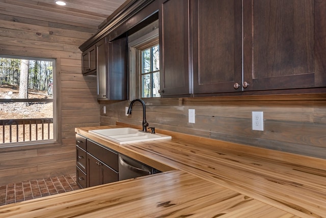 kitchen featuring wood walls, dark brown cabinetry, sink, and butcher block countertops