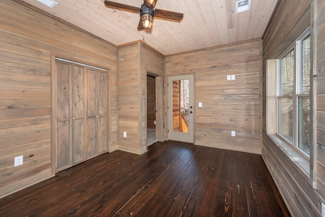 empty room featuring ceiling fan, dark wood-type flooring, wooden ceiling, and wooden walls