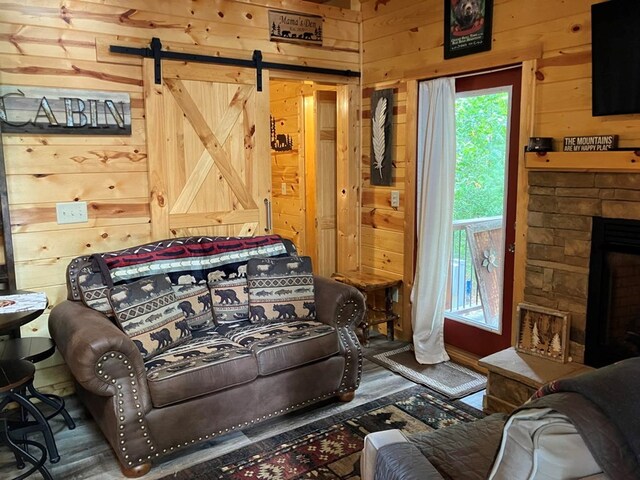 living room with a stone fireplace, wood walls, a barn door, and dark hardwood / wood-style floors