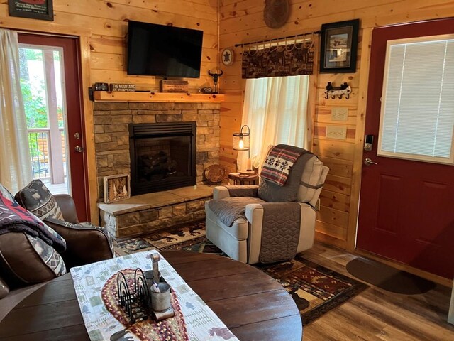 living room featuring wood walls, hardwood / wood-style flooring, and a stone fireplace