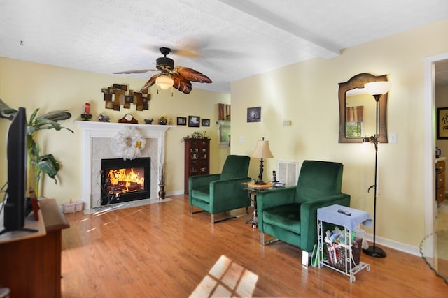 living area featuring a textured ceiling, ceiling fan, beam ceiling, a premium fireplace, and hardwood / wood-style floors