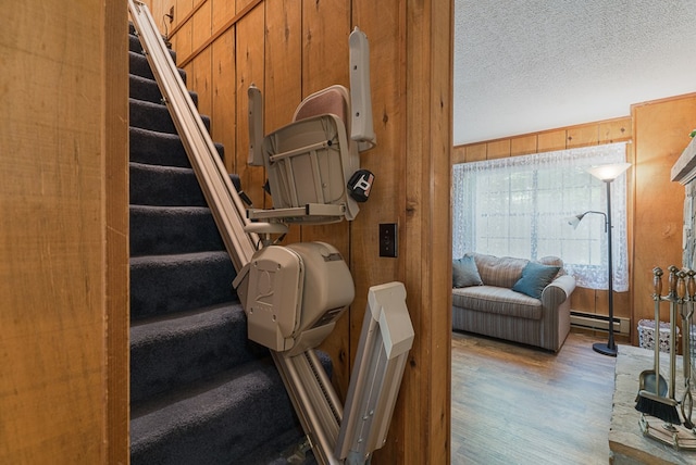 staircase featuring wood walls, wood-type flooring, baseboard heating, and a textured ceiling