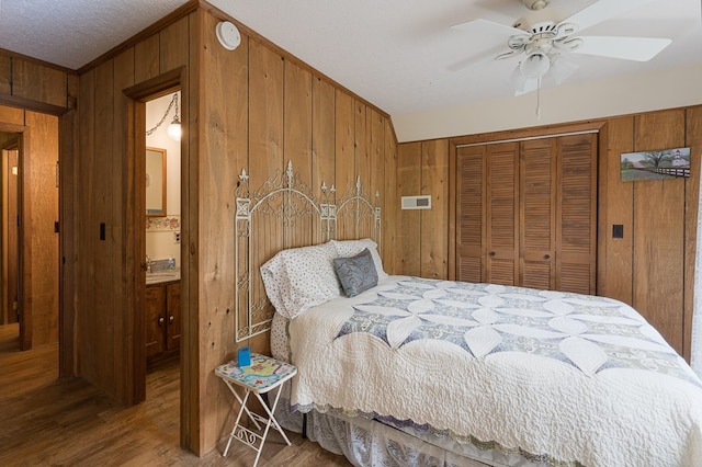 bedroom featuring a textured ceiling, wood walls, ceiling fan, a closet, and dark wood-type flooring