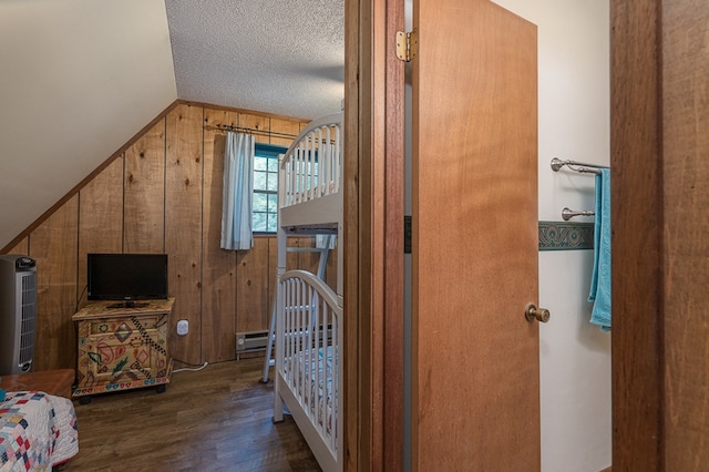 bedroom with a textured ceiling, vaulted ceiling, dark wood-type flooring, baseboard heating, and wooden walls