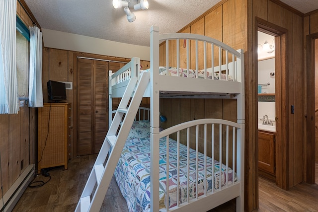 bedroom featuring a textured ceiling, wood walls, hardwood / wood-style floors, a closet, and baseboard heating