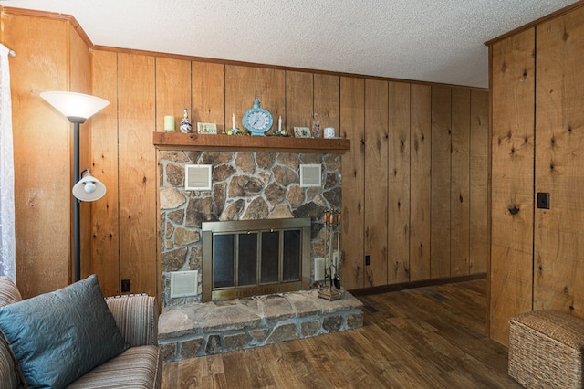 living room with a textured ceiling, dark hardwood / wood-style floors, a stone fireplace, and wooden walls