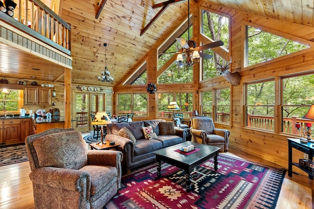 living room featuring ceiling fan with notable chandelier, high vaulted ceiling, wooden walls, and light hardwood / wood-style floors