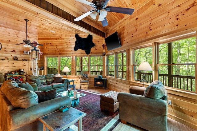 sunroom featuring lofted ceiling, ceiling fan, a wood stove, and wood ceiling