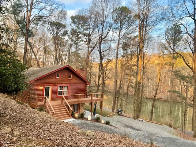 exterior space with driveway, a chimney, log siding, and a wooden deck