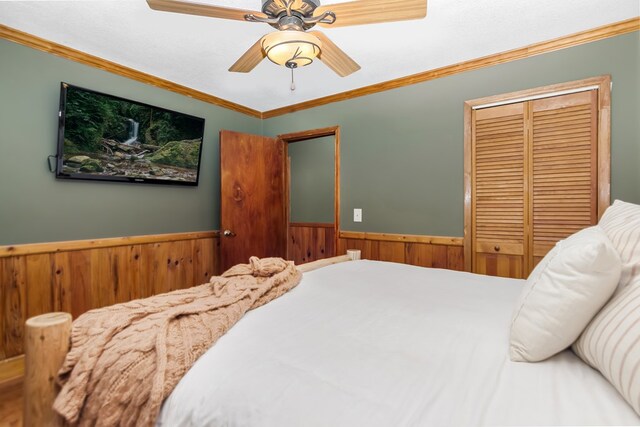 bedroom featuring a closet, ornamental molding, wainscoting, wood walls, and ceiling fan