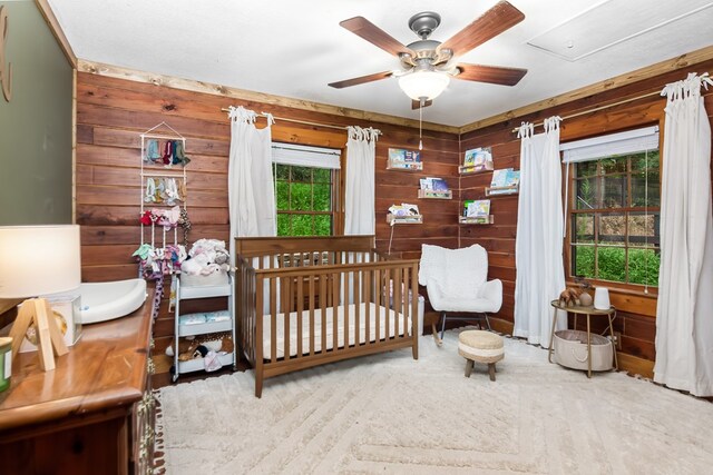 bedroom featuring hardwood / wood-style flooring, a nursery area, ceiling fan, and wood walls