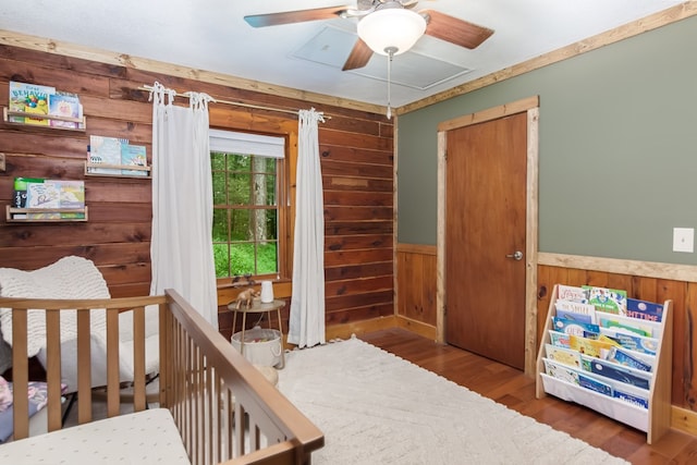 bedroom featuring a wainscoted wall, wooden walls, a ceiling fan, and wood finished floors