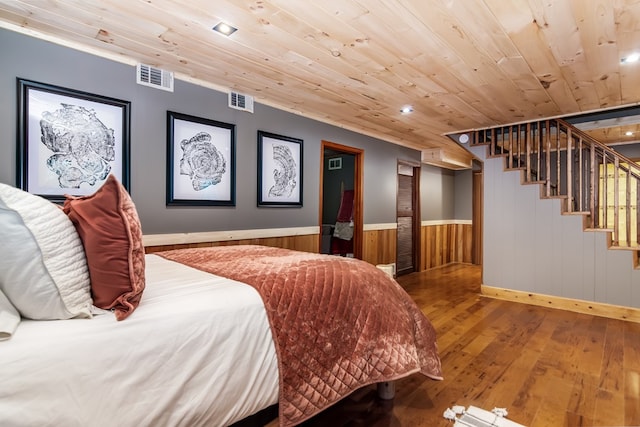 bedroom with crown molding, hardwood / wood-style floors, wooden ceiling, and wooden walls