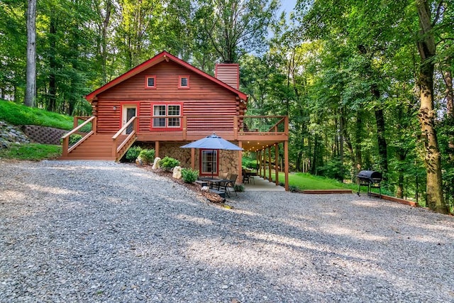 view of front of house featuring a deck, stone siding, a chimney, and log siding