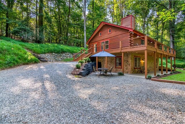 view of front facade with a patio, stairs, stone siding, log exterior, and a chimney