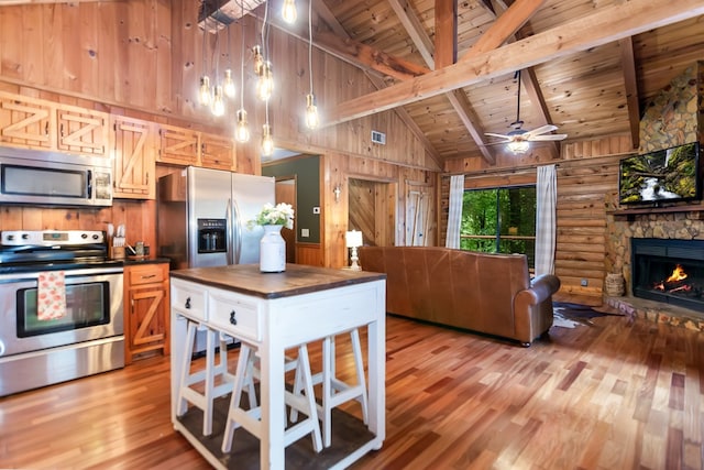 kitchen with wooden walls, wood ceiling, open floor plan, appliances with stainless steel finishes, and beam ceiling