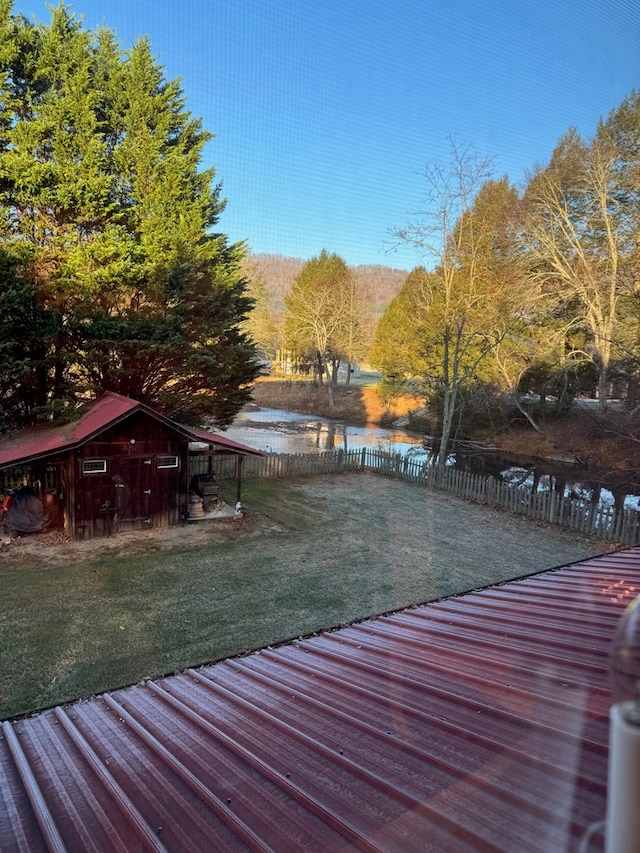 wooden terrace featuring a water view, fence, and a lawn