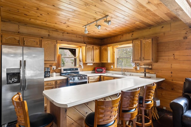 kitchen with track lighting, a peninsula, appliances with stainless steel finishes, a sink, and light countertops