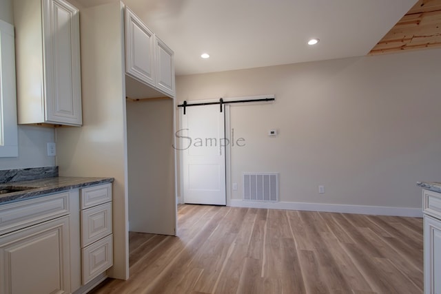 kitchen featuring white cabinetry, a barn door, dark stone countertops, and light hardwood / wood-style flooring