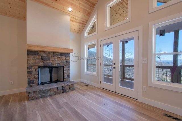 unfurnished living room featuring wood ceiling, light hardwood / wood-style flooring, high vaulted ceiling, a fireplace, and a wealth of natural light