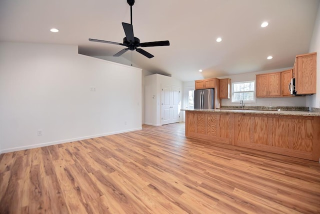 kitchen with kitchen peninsula, light stone counters, stainless steel appliances, light hardwood / wood-style floors, and lofted ceiling