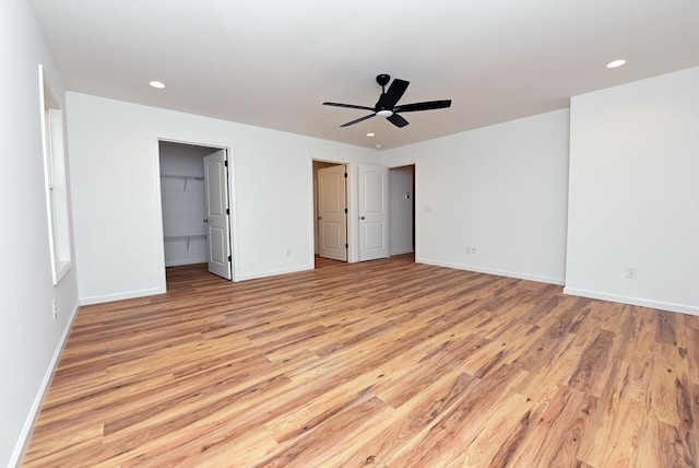 unfurnished bedroom with a walk in closet, ceiling fan, a closet, and light wood-type flooring