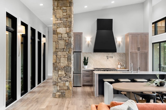 kitchen with ornate columns, tasteful backsplash, ventilation hood, light wood-type flooring, and stainless steel appliances