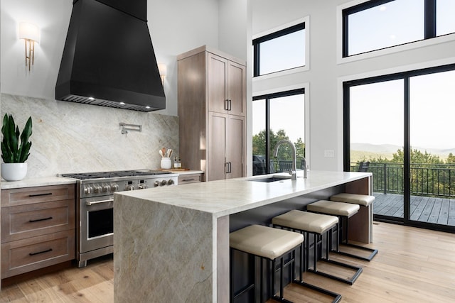 kitchen with sink, a breakfast bar, high end stainless steel range oven, an island with sink, and custom range hood