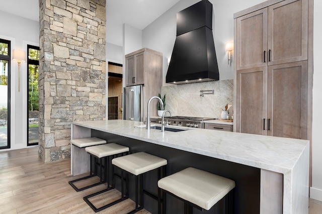 kitchen featuring sink, light stone countertops, decorative backsplash, custom exhaust hood, and high end refrigerator