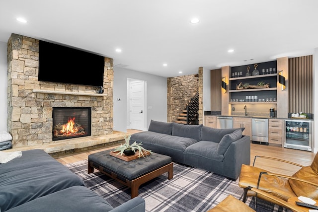 living room with a stone fireplace, indoor wet bar, wine cooler, and light wood-type flooring