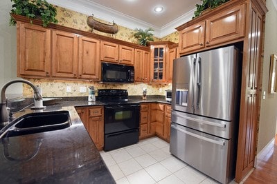 kitchen featuring light tile patterned floors, ornamental molding, sink, black appliances, and dark stone counters