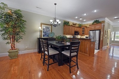 dining room with light wood-type flooring, ornamental molding, and a notable chandelier