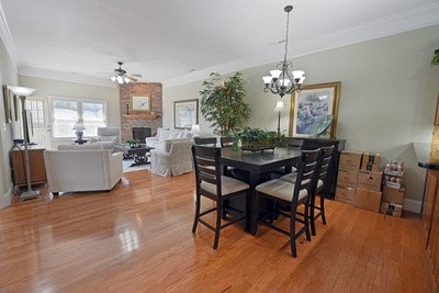 dining room with ceiling fan with notable chandelier, light hardwood / wood-style flooring, a fireplace, and crown molding