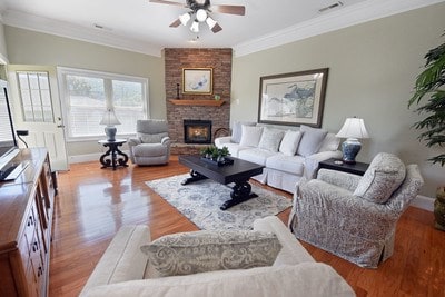 living room with light wood-type flooring, crown molding, a large fireplace, and ceiling fan