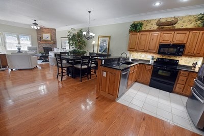 kitchen featuring ceiling fan with notable chandelier, kitchen peninsula, black appliances, decorative light fixtures, and sink