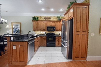 kitchen with pendant lighting, a chandelier, kitchen peninsula, black appliances, and crown molding