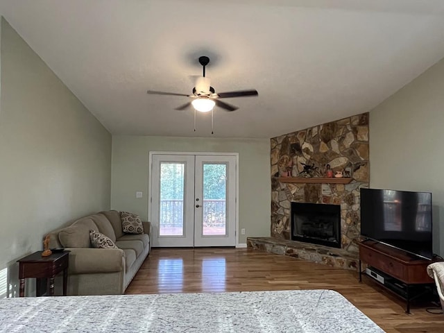 living room featuring hardwood / wood-style flooring, ceiling fan, a fireplace, vaulted ceiling, and french doors