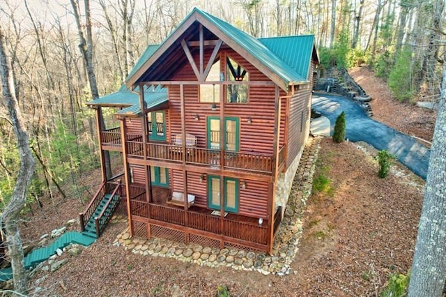 rear view of property featuring faux log siding, a deck, a forest view, french doors, and metal roof