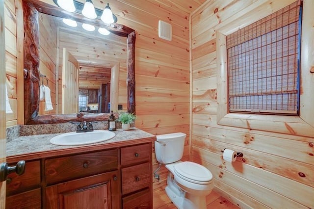 half bathroom featuring toilet, wood walls, and vanity