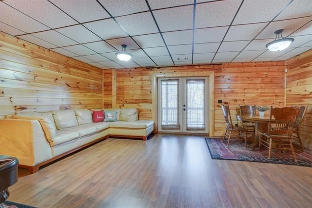 unfurnished living room featuring a paneled ceiling, wood walls, french doors, and wood finished floors