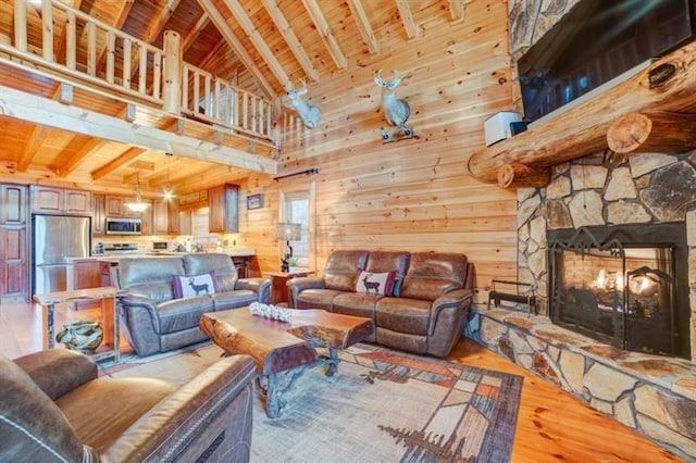 living room with wooden ceiling, a stone fireplace, a towering ceiling, and light wood-type flooring