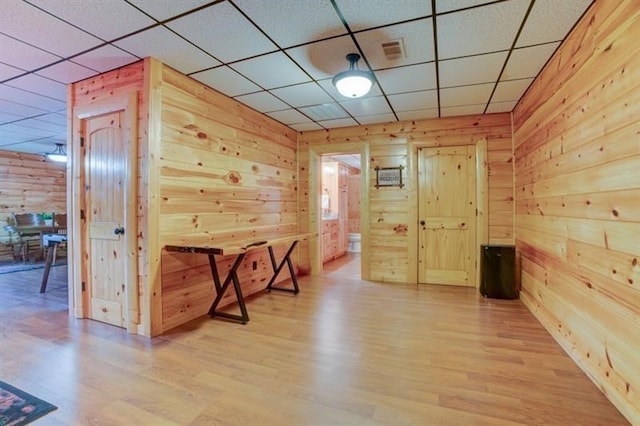 interior space featuring light wood finished floors, wood walls, a paneled ceiling, and visible vents