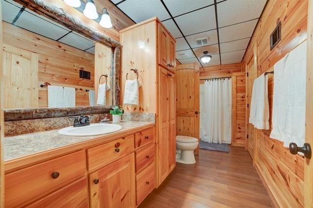 bathroom with wooden walls, vanity, toilet, and visible vents