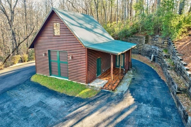 exterior space with log veneer siding, metal roof, an outdoor structure, and aphalt driveway